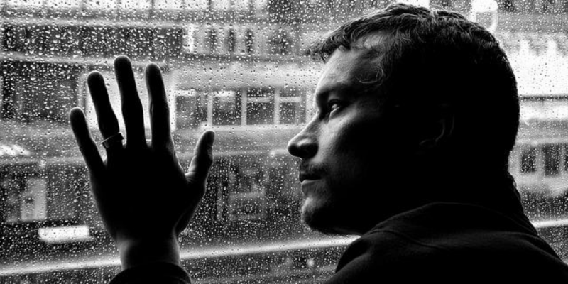 Depressed man looking out the window, feeling sad because he has no social life.